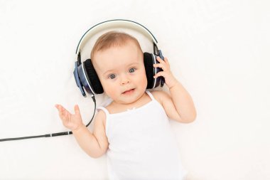 Küçük bir kız çocuğu. 6 aylık. Kulaklıkla yatakta uzanıp müzik dinliyor.