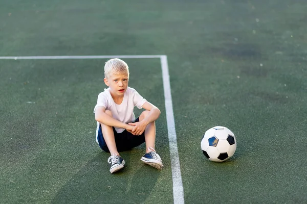 Menino Loiro Uniforme Esportivo Senta Campo Futebol Com Uma Bola — Fotografia de Stock