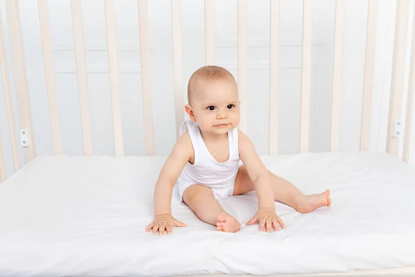 8个月大的男婴穿着白衣坐在儿童房的婴儿床里 看着摄像机 就是婴儿出生的那天早上 — 图库照片