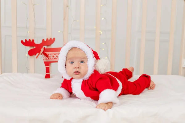 baby 6 months in a Santa costume lying in a crib at home on his stomach, a gift for the new year. Christmas holiday concept
