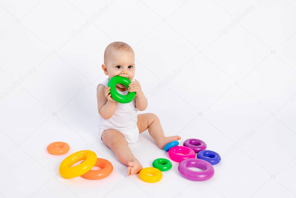 cute boy 8 months old playing with a pyramid on a white isolated background and licking toys, place for text, early development of children