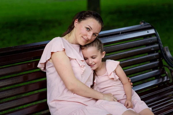 mother and daughter 5-6 years old walk in the Park in the summer, mother hugs her daughter sitting on a bench, the concept of a happy family, the relationship of mother and child, mother\'s day