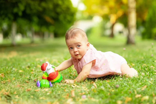 ピンクのボディスーツに身を包んだ緑の芝生で7ヶ月の少女は新鮮な空気の中を歩き — ストック写真