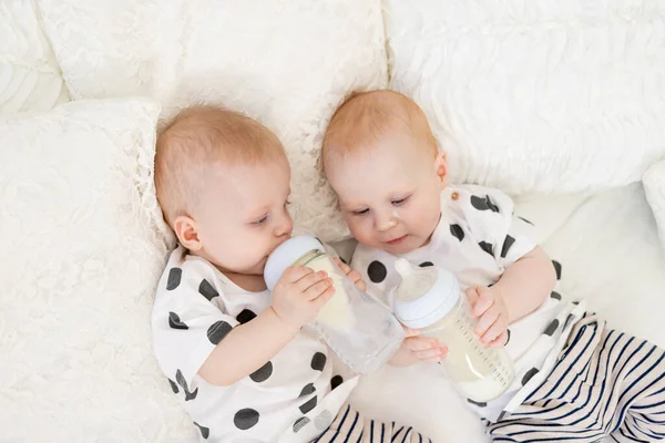 两个双胞胎宝宝的兄妹8个月大穿着睡衣躺在床上 喝着瓶子里的牛奶 吃婴儿食品的概念 高瞻远瞩 友谊的概念 发短信的地方 — 图库照片