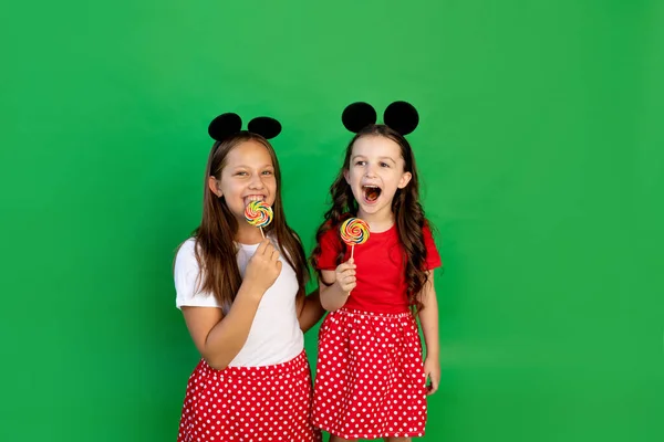 穿着红色衣服的可爱小女孩和米老鼠耳朵在绿色孤立的背景上吃着大棒棒糖 文本空间 庆祝和销售的概念 — 图库照片