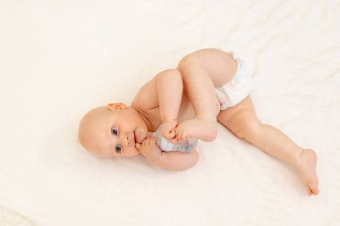 8 aylık bebek bezi içinde beyaz bir yatakta yatıyordu. Ev bacağında bir şişe süt vardı. Top view, bebek maması konsepti, biberondan bebek içme suyu, mesaj atmak için yer.