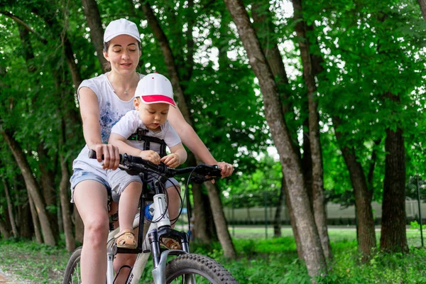 mother and son ride a Bicycle, mother carries a child in a child's chair on a Bicycle in the Park in the summer