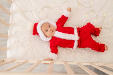 Noel Baba kostümlü bir bebeğin Noel fotoğrafı. Evdeki bir karyolada yatıyor. Üst manzara, mutlu yıllar. Noel tatili kavramı