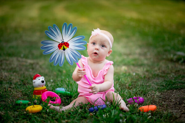baby girl 10 months old sitting on the grass in the summer and playing with a turntable, early development of children, outdoor games