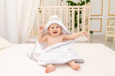 Bebek 8 aylık beyaz bir yatakta beyaz bir havluyla banyoda banyo yaptıktan sonra ağladı.