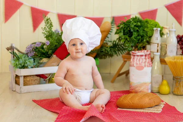 a baby in a cook\'s hat sits in a beautiful photo zone with flour and vegetables, a baby cook, a child with flour and bread prepares food