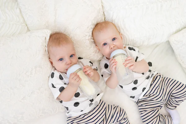 two baby twins brother and sister 8 months old lie on the bed in their pajamas and drink milk from a bottle, baby food concept, top view, concept of friendship, place for text
