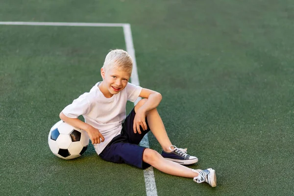 Menino Loiro Uniforme Esportivo Senta Campo Futebol Com Uma Bola — Fotografia de Stock