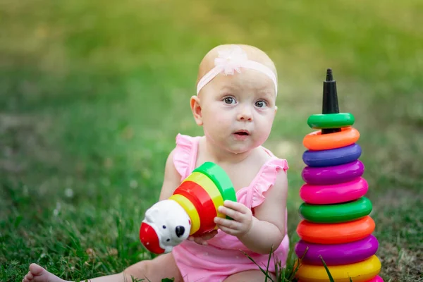 Yazın çimlerin üzerinde oturan ve piramit oynayan 10 aylık bir bebek. Çocukların erken gelişimi, açık hava oyunları.