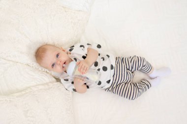 Bebek 8 aylıkken pijamayla yatağa uzanıp şişeden süt içerken, bebek maması konsepti, üst manzara, mesaj atmak için yer