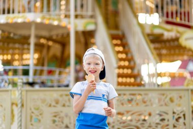5-6 yaşındaki mutlu çocuk lunaparkta yürüyor ve dondurma yiyor. Çocuk yaşam tarzı