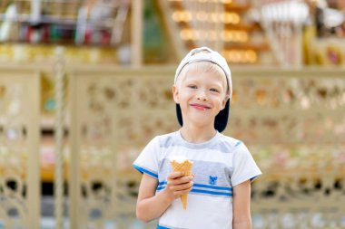 5-6 yaşındaki mutlu çocuk lunaparkta yürüyor ve dondurma yiyor. Çocuk yaşam tarzı