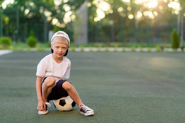 Menino Loiro Boné Uniforme Esportivo Senta Uma Bola Futebol Campo — Fotografia de Stock