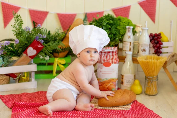 a baby in a cook\'s hat sits in a beautiful photo zone with flour and vegetables, a baby cook, a child with flour and bread prepares food