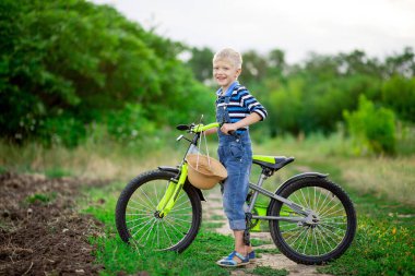 Bisikletli mutlu sarışın erkek bebek yazın bir tarlada duruyor, çocuk yaşam tarzı.