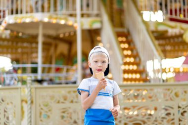 5-6 yaşındaki mutlu çocuk lunaparkta yürüyor ve dondurma yiyor. Çocuk yaşam tarzı
