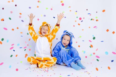 Parlak kostümlü küçük çocuklar beyaz bir arka planda oturur ve konfetileri uçurur, çocukların doğum günlerini, mesajlaşma yerlerini.