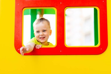 Oyun bahçesinde oynayan küçük mutlu çocuk, pencereden dışarı bakan çocuk, çocuk yaşam tarzı.