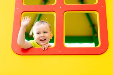 Oyun bahçesinde oynayan küçük mutlu çocuk, pencereden dışarı bakan çocuk, çocuk yaşam tarzı.