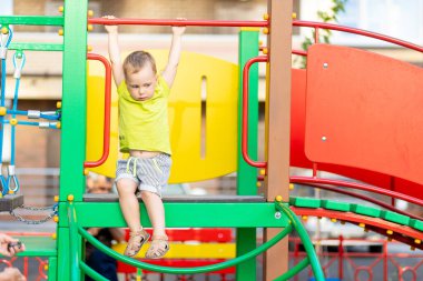 Şirin 3 yaşındaki çocuk serin bulutlu bir günde sarı bir oyun parkında heyecanlı bir şekilde oynuyor.