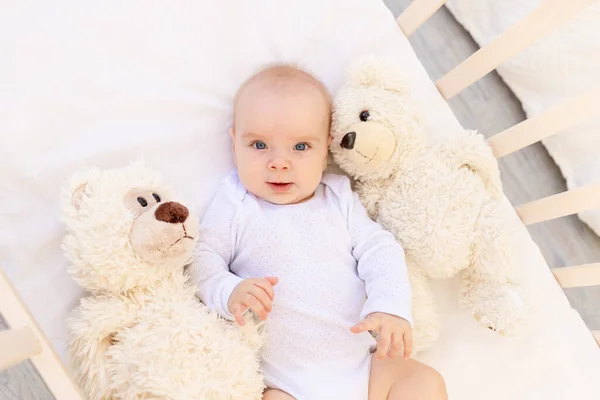 一个小孩的画像一个6个月大的穿着白色紧身衣的女孩躺在小孩床上躺着柔软的玩具熊 — 图库照片