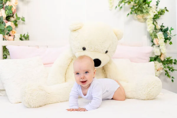 一个6个月大的小女孩和一只大灰熊躺在家里的一张白色的床上 — 图库照片