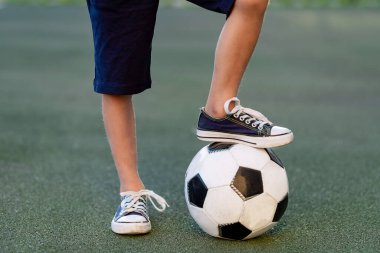 Futbol sahasında yeşil bir çimenlikte futbol topuyla, spor bölümünde antrenman yapan bir çocuğun ayakları.