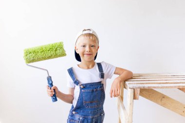 Çocuk inşaatçı beyaz duvarlı bir dairede tamirat yapıyor. Bir işçi duvarları silindirle boyamak istiyor.