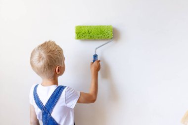 Çocuk inşaatçı bir dairede beyaz duvarları silindirle boyuyor, bir çocuk evi tamir ediyor, dikiz manzarası, mesaj atmak için yer arıyor.