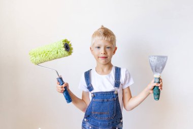Çocuk inşaatçı inşaat aletlerini beyaz duvarları olan bir dairede tutuyor, çocuk duvarları boyuyor, yazı için yer, tamir konsepti.