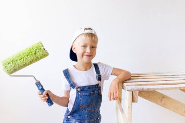 Çocuk inşaatçı beyaz duvarlı bir dairede tamirat yapıyor. Bir işçi duvarları silindirle boyamak istiyor.