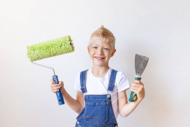 Bir çocuk inşaatçı, beyaz duvarlı bir dairede inşaat aletleri bulundurur, sarı saçlı bir çocuk duvarları boyar, yazı yazacak bir yer, tamir konsepti.