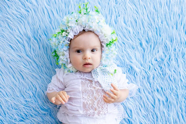 美しい少女が花でできた帽子に青いふわふわの絨毯の上に横たわってカメラを見ると — ストック写真