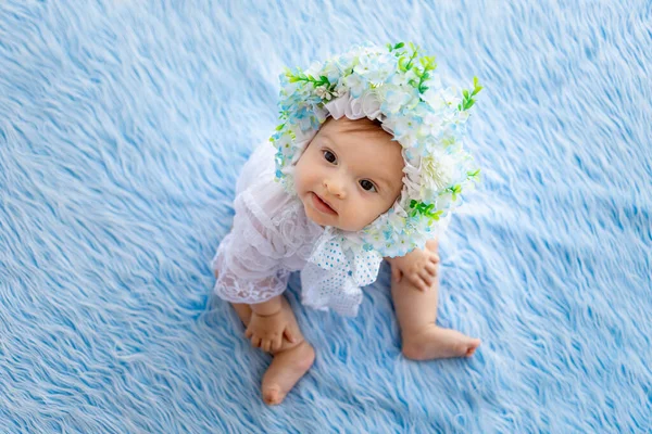 美しい少女が花でできた帽子に青いふわふわの絨毯の上に座ってカメラを見ると — ストック写真