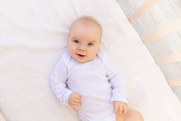 一个6个月大的小女孩的画像 穿着白色的紧身衣躺在白色的床上 上面有文字 — 图库照片