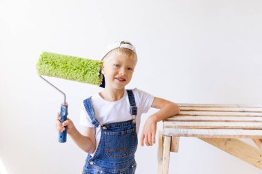 Çocuk inşaatçı beyaz duvarlı bir dairede tamirat yapıyor. Bir işçi duvarları silindirle boyamak istiyor.