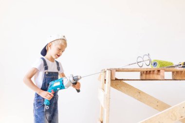 Bir çocuk inşaatçı, arka planda beyaz bir duvar ve bir inşaat merdiveni, metin için bir yer, bir inşaat ve onarım konsepti ile bir yapı mikseri bulundurur.