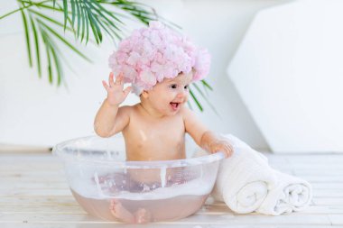 Küçük mutlu kız evdeki parlak bir odada, çiçeklerden yapılmış güzel bir boneyle köpük ve suyla bir havuzda yıkanıyor.