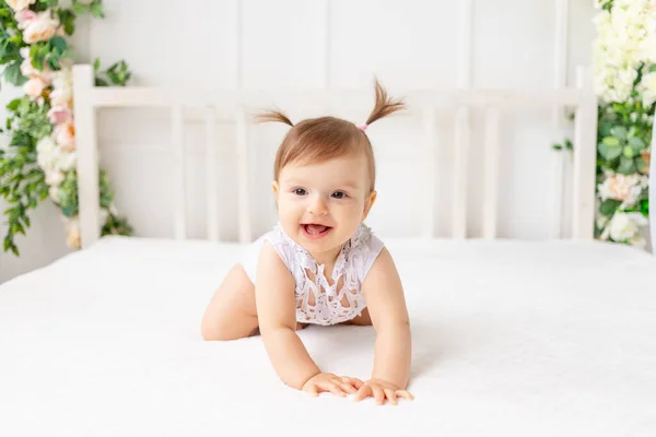 6个月大的小女孩坐在一个明亮美丽的房间里 穿着花边紧身衣 躺在白色的床上 面带微笑 看上去很滑稽 — 图库照片