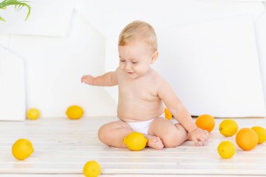 Küçük bir çocuk. Altı aylık bir çocuk. Parlak beyaz bir odada limon ve portakallı bezlerle yerde oynuyor.