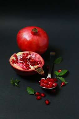 Karanlık arka planda izole edilmiş sulu nar meyvesi. Koyu arkaplanda kırmızı nar suyu. Koyu arkaplanda yaprakları olan olgun bir nar.