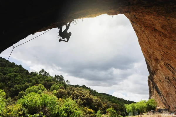 Silhouette of a young man climbing a collapsed wall inside a cave. Cloudy sky background.