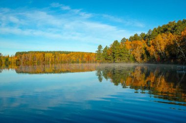 Sonbahar ağaçları mavi göl sularını yansıtır. Yatay sonbahar manzarası