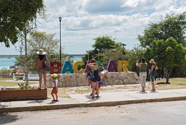 BACALAR, MEXICO-MARCH 07, 2018: photographing tourists in front of the colored lettering bacalar, quintana roo, mexico clipart