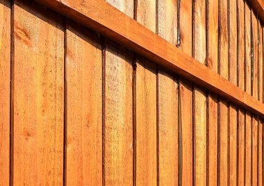 A section of brown, vertical, overlapped wooden garden fence in closeup in the sun with shadows clipart